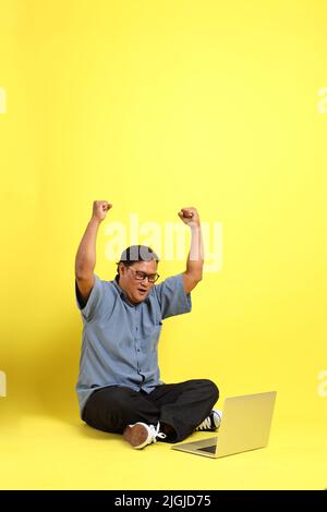 L'uomo asiatico adulto con camicia blu seduta su sfondo giallo. Foto Stock