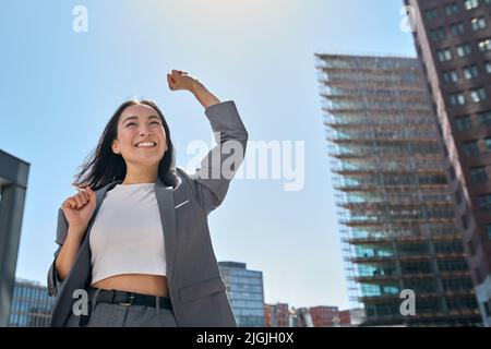 Giovane entusiasta fiduciosa donna asiatica d'affari che sente vincitore nella grande città. Foto Stock
