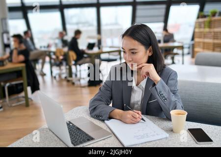 Giovane donna asiatica d'affari che usa il laptop che lavora in un grande ufficio moderno. Foto Stock