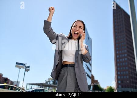 Giovane donna d'affari asiatica allegra che parla sul cellulare ridendo sulla strada della città. Foto Stock