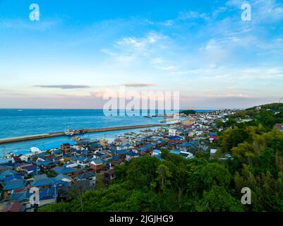 Vista aerea della piccola cittadina di pescatori giapponese con nubi al tramonto sullo sfondo Foto Stock