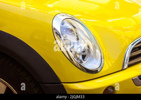 Madrid, Spagna. Giugno 7, 2022. Faro anteriore ovale di moderna elegante vettura gialla. Sedan automobile MINI Cooper Countryman in su da vicino. Settore automobilistico. Foto Stock