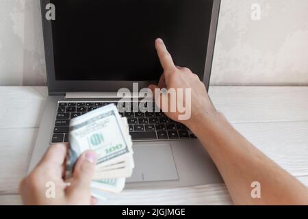 L'uomo mostra qualcosa sullo schermo del portatile con soldi Foto Stock