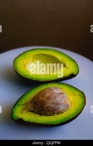 Due fette di avocado biologico appena sfornato e maturo su un tagliere bianco. Messa a fuoco selettiva. Foto Stock