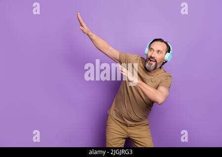 Foto di un uomo allegro ed energico di mezza età che si sente giovane ballare dab ascoltare musica in cuffia isolato su sfondo di colore viola Foto Stock