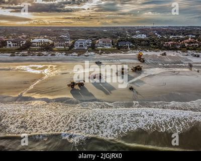 Foto aerea del drone di Caterpillar Trucks che restaurano le dune a Ponte Vedra Beach, Florida, St. Johns County, con case sul lungomare e un vibrante cielo al tramonto. Foto Stock