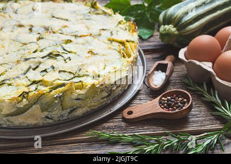 Torta di zucchine fatta in casa, al forno con parmigiano, uova ed erbe sul tavolo in legno da vicino Foto Stock