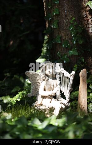 Una statua giardino di una fata con un'arpa seduta nei boschi tra le viti e vicino ad un albero in primavera o estate, Lancaster, Pennsylvania Foto Stock