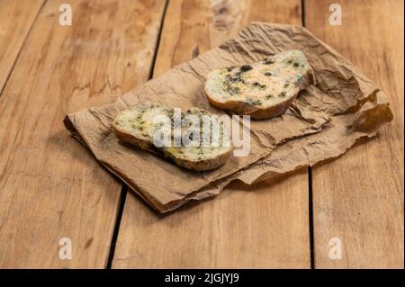 Pane ammuffito su sfondo di legno. Due fette di pane di grano coperto di muffa fungina. Il pane si trova sopra un sacchetto di carta marrone. Cibo guastato. S Foto Stock