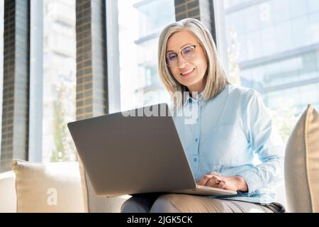 Donna anziana lavora come freelance su un notebook in un collegio. Foto Stock