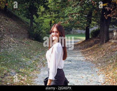 Scena autunnale. Giovane donna allegra in gonna e camicia passeggiate nel parco naturale su un tramonto. Concetto di moda e stile. Concetto di gente di tempo libero e di stagione. Loc Foto Stock