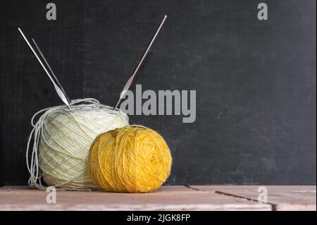 rotoli di filo di lana giallo e bianco, pronti per iniziare l'uncinatura, posti su fondo di legno nero e arancio, rotolo di filo a tre crochet d'acciaio Foto Stock