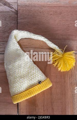 cappello di elfo giallo e bianco per l'inverno, accovacciato a mano su sfondo di legno arancione. cappello fatto in casa da una donna intraprendente. concetto di entrep Foto Stock