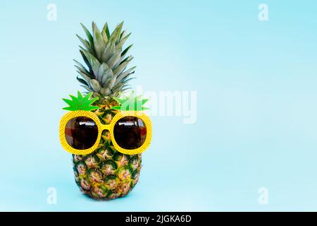Ananas divertente in un bicchiere di ananas a forma di sfondo blu. Estate in stile tropicale sulle vibrazioni della spiaggia. Frutta esotica. Resort vacanza crea Foto Stock