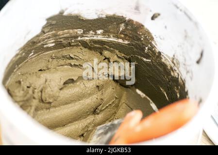 Mescolando cemento ed acqua in un contenitore per ottenere la miscela finita. Processo di costruzione, una delle fasi di finitura. Produzione di gesso. Costruzione Foto Stock