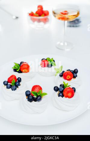 Primo piano torta meringa Pavlova con fragole fresche e mirtilli con menta sul piatto bianco e cocktail con fragola. Dessert e. Foto Stock