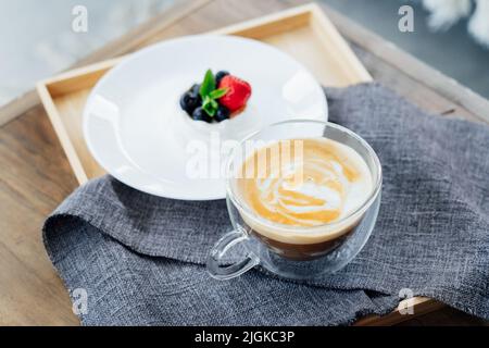 Il mini nido per dolci Pavlova e una tazza di caffe' latte sul vassoio di legno con tovagliolo grigio sul tavolo. Ora del caffè. Per fare una pausa e rilassarsi. SEL Foto Stock