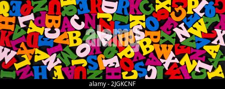 Lettere colorate in legno chiaro su sfondo nero banner. Concetto di ritorno a scuola. Foto Stock