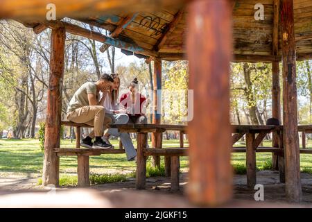 Due amici felici che guardano contenuti multimediali in smartphone seduti sulla panca di un parco Foto Stock