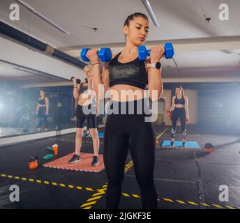 Gruppo di giovani donne atletiche in abbigliamento sportivo con manubri in esercizio in palestra Foto Stock