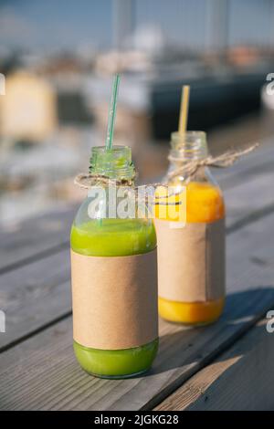 Due bottiglie di succo o frullati si trovano su un tavolo o sfondo di legno. Succo d'arancia e kiwi. Cocktail di frutta in un ristorante sulla spiaggia di mare. Vitamina Foto Stock