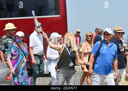 Oia, Santorini, Grecia - Giugno 2022: Guida turistica che conduce un gruppo di turisti attraverso una strada su Sanotini. Alcune persone indossano maschere Foto Stock