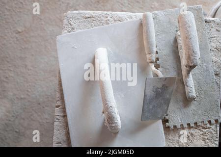Gli strumenti usati per i muratori giacciono su un tavolo. Lo strumento è bianco e pieno di colore. Anche il tavolo è bianco. Foto Stock