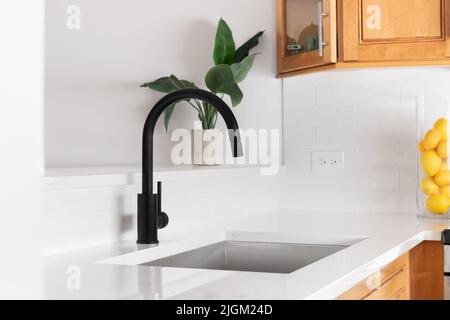 Un dettaglio lavandino della cucina girato con piano di lavoro in marmo bianco, rubinetto nero, e mobili in legno. Foto Stock