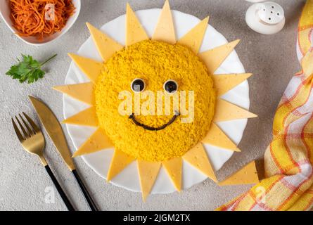 Insalata a forma di sole, con pollo, uova, carote e formaggio su sfondo grigio chiaro. Un'idea culinaria per le feste dei bambini Foto Stock