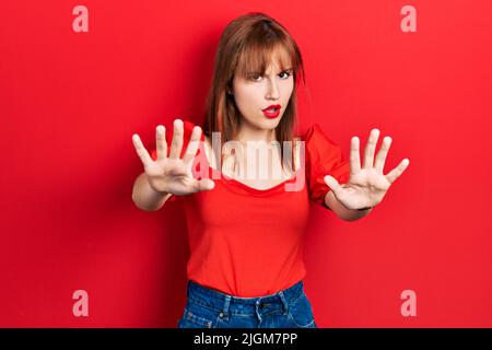 Giovane donna rossa che indossa casual t shirt rossa facendo stop gesture con mani palme, arrabbiato e espressione di frustrazione Foto Stock