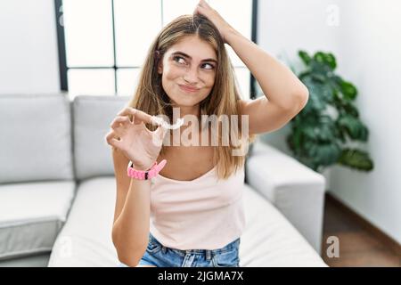 Giovane donna bionda che tiene invisibile aligner ortodontico confondersi e si chiede circa domanda. Incerto con dubbio, pensando con mano sulla testa. pensi Foto Stock