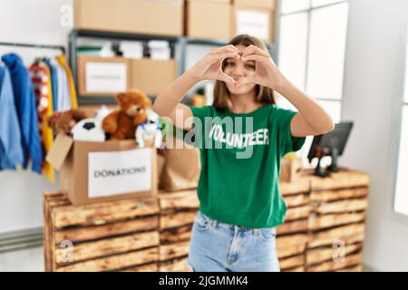 Adorabile ragazza che indossa uniforme volontaria facendo il simbolo del cuore con le mani al centro di carità Foto Stock