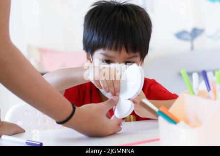 Piccolo capretto che tiene la carta della farfalla. Asia ragazzo studente imparare a creare la carta fai da te farfalla da insegnante in scuola materna alla scuola materna Foto Stock