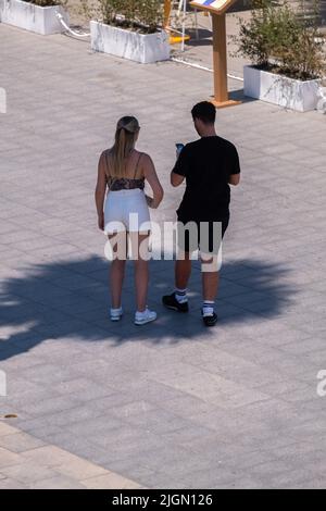 Barcellona, Spagna. 11th luglio 2022. Una coppia turistica è visto consultare il loro dispositivo mobile sotto l'ombra di una palma sulla spiaggia di Sant Sebantian. Seconda ondata di calore estremo che può superare i 44 gradi Celsius in alcune regioni della Spagna. La Catalogna, attualmente al livello uno e dopo settimane di accumulo di alte temperature e di poca pioggia, soffrirà questa settimana alcuni giorni di temperature al di sopra di quanto è solito per queste date Credit: SOPA Images Limited/Alamy Live News Foto Stock