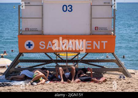Barcellona, Spagna. 11th luglio 2022. Un gruppo di persone ha visto rifugio sotto l'ombra della capanna di salvataggio spiaggia. Seconda ondata di calore estremo che può superare i 44 gradi Celsius in alcune regioni della Spagna. La Catalogna, attualmente al livello uno e dopo settimane di accumulo di alte temperature e di poca pioggia, soffrirà questa settimana alcuni giorni di temperature al di sopra di quanto è solito per queste date Credit: SOPA Images Limited/Alamy Live News Foto Stock