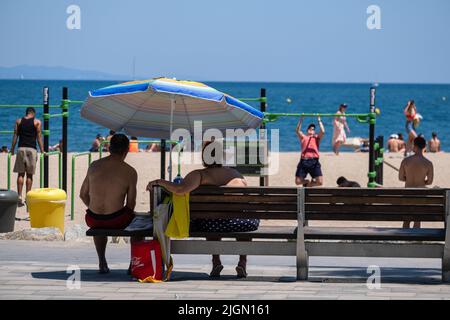 Barcellona, Spagna. 11th luglio 2022. Una coppia è vista sulla spiaggia di Sant Sebastian seduto su una panca pubblica protetta dal sole da un ombrello. Seconda ondata di calore estremo che può superare i 44 gradi Celsius in alcune regioni della Spagna. La Catalogna, attualmente al livello uno e dopo settimane di accumulo di alte temperature e di poca pioggia, soffrirà questa settimana alcuni giorni di temperature al di sopra di quanto è solito per queste date Credit: SOPA Images Limited/Alamy Live News Foto Stock