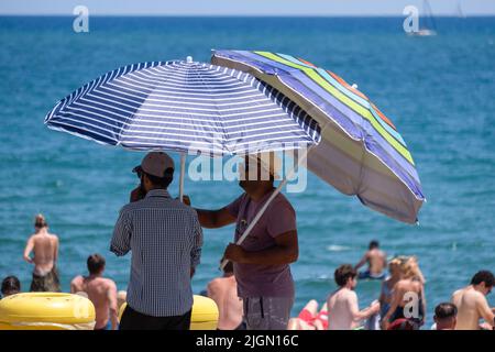Barcellona, Spagna. 11th luglio 2022. Sulla spiaggia di Barceloneta si possono vedere dei venditori di ombrelloni. Seconda ondata di calore estremo che può superare i 44 gradi Celsius in alcune regioni della Spagna. La Catalogna, attualmente al livello uno e dopo settimane di accumulo di alte temperature e di poca pioggia, soffrirà questa settimana alcuni giorni di temperature al di sopra di quanto è solito per queste date Credit: SOPA Images Limited/Alamy Live News Foto Stock