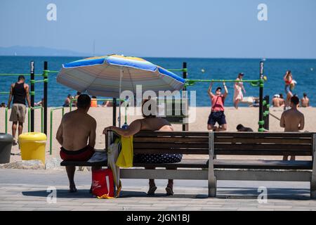 Barcellona, Spagna. 11th luglio 2022. Una coppia è vista sulla spiaggia di Sant Sebastian seduto su una panca pubblica protetta dal sole da un ombrello. Seconda ondata di calore estremo che può superare i 44 gradi Celsius in alcune regioni della Spagna. La Catalogna, attualmente al livello uno e dopo settimane di accumulo di alte temperature e di poca pioggia, soffrirà questa settimana alcuni giorni di temperature al di sopra di quanto è solito per queste date (Foto di Paco Freire/SOPA Images/Sipa USA) Credit: Sipa USA/Alamy Live News Foto Stock