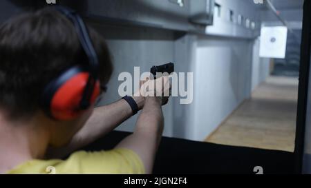 Guy in cuffie tattiche puntando la pistola al bersaglio nel campo di tiro Foto Stock