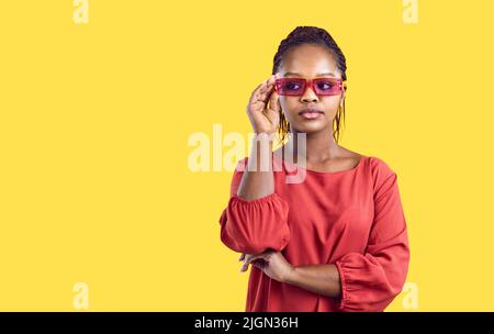 Ritratto di giovane afroamericana fresca ed elegante in bicchieri rossi su sfondo giallo. Foto Stock