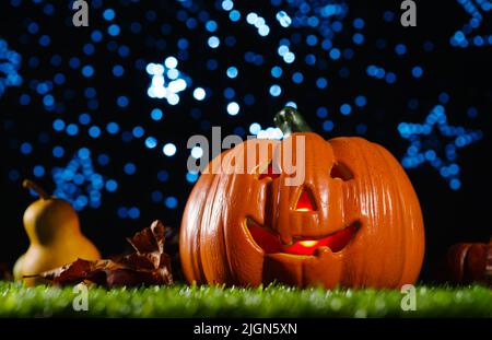 Il simbolo della festa autunnale di Halloween è una zucca arancione sorridente che risplendono dall'interno su erba verde sullo sfondo di una stella scintillante Foto Stock