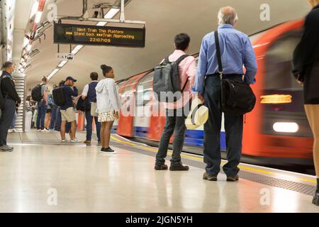 I pendolari dalla città di Londra aspettano sulla piattaforma alla stazione della banca come un treno della metropolitana che si avvicina alla piattaforma London England UK Foto Stock