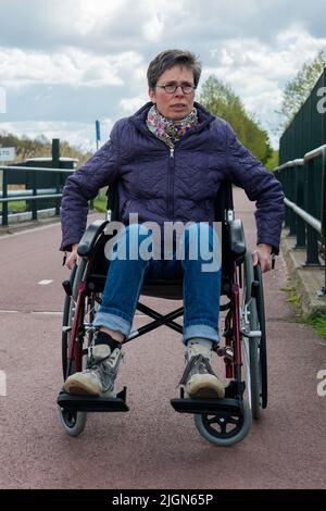 Tilburg, Paesi Bassi. Femmina di sclerosi multipla che si occupano del paziente con la sua condizione di on e off mediante una sedia a rotelle per ottenere lungo. Foto Stock