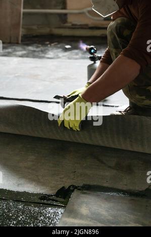 L'operatore svita il rullo di impermeabilizzazione e lo fissa alla resina, installando impermeabilizzazione. Foto Stock