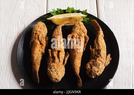 Gustoso pesce fritto su piatto nero, vista dall'alto Foto Stock