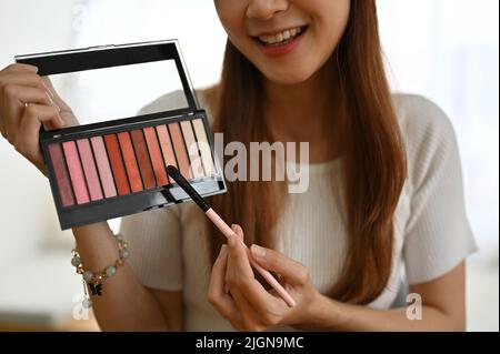 Attraente blogger di bellezza femminile millennial asiatico mostrando una tavolozza di eyeshadow, rivedendo i prodotti cosmetici e facendo un video di trucco. Foto Stock
