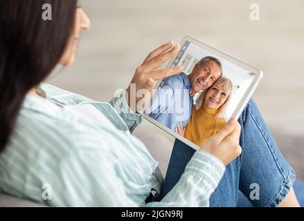 Giovane donna che tiene un tablet digitale e videochiama i genitori senior Foto Stock