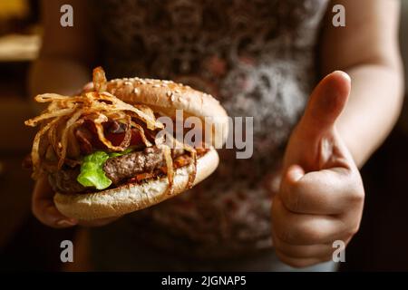 Donna incinta irriconoscibile godere il suo hamburger Foto Stock