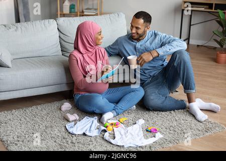 Una coppia musulmana incinta nera che fa la lista di controllo delle necessità, preparandosi per il parto Foto Stock