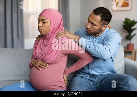 Amorevole marito che fa il massaggio alla sua moglie nera incinta musulmana a casa Foto Stock